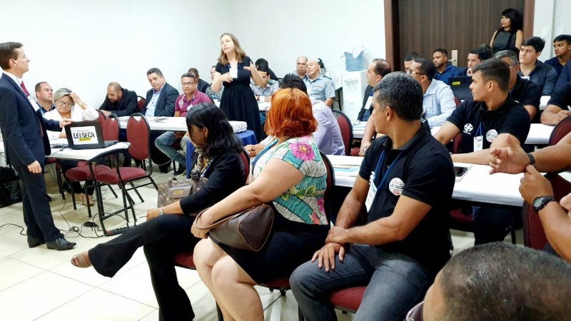 Foto de uma sala onde se encontram sentados o público participante do Fórum das operações da Lei Seca do Brasil. Luciane Ninki, do DetranRS, está em pé falando, observada por Francisco Garonce, do Denatran