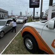 Foto horizontal colorida mostra o cenário de uma avenida movimentada com a vitura da Balada Segura parada no canteiro e agentes conversando com motoristas pela janela dos carros