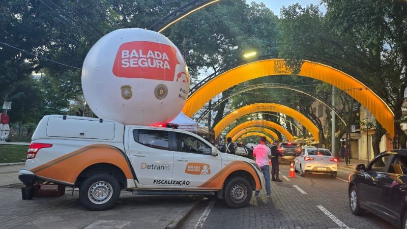 Avenida de santa cruz do sul com arcos amarelos. Caminhonete de Balada Segura em primeiro plano com balão da Balada sobre. Agentes de costas trabalham em blitze educativa.