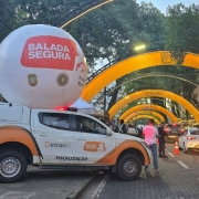 Avenida de santa cruz do sul com arcos amarelos. Caminhonete de Balada Segura em primeiro plano com balão da Balada sobre. Agentes de costas trabalham em blitze educativa.